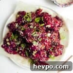 Pile of crispy Korean fried chicken on a small white plate with sesame seeds on the side.