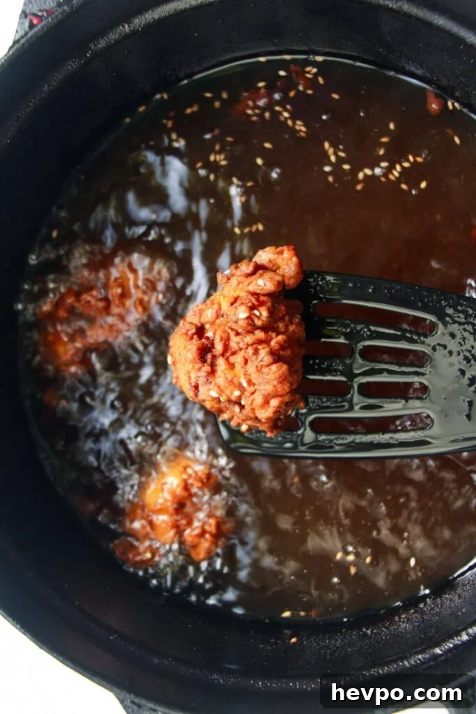 Crispy Korean Fried Chicken Recipe: Extra Crunch & Sticky Sauce 9 Spatula holding up a piece of golden fried chicken with more chicken in the background.