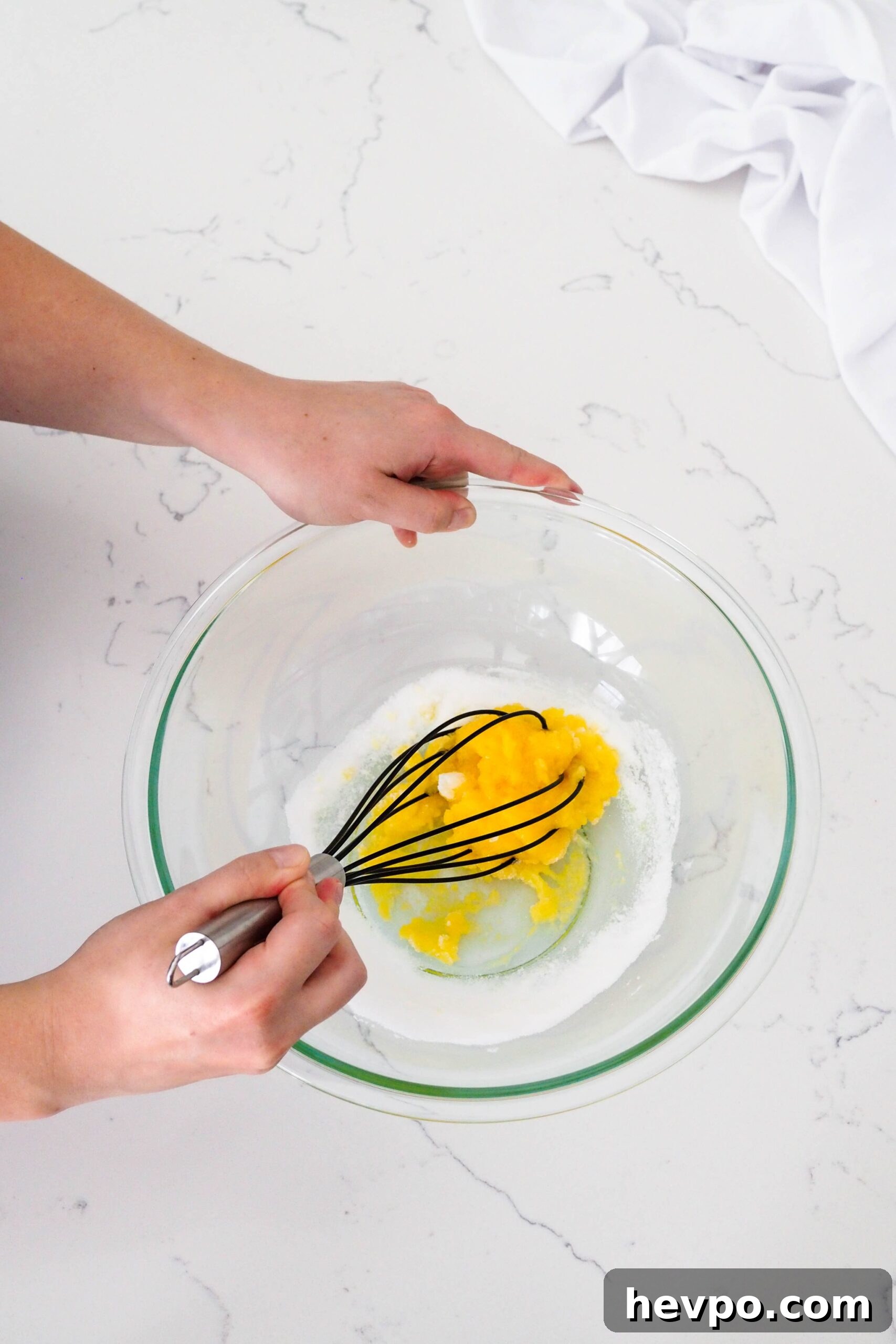 Homemade French Vanilla Ice Cream Recipe – Creamy & Classic 4 Two hands whisk together a dense and bright yellow mixture of egg yolks and sugar.