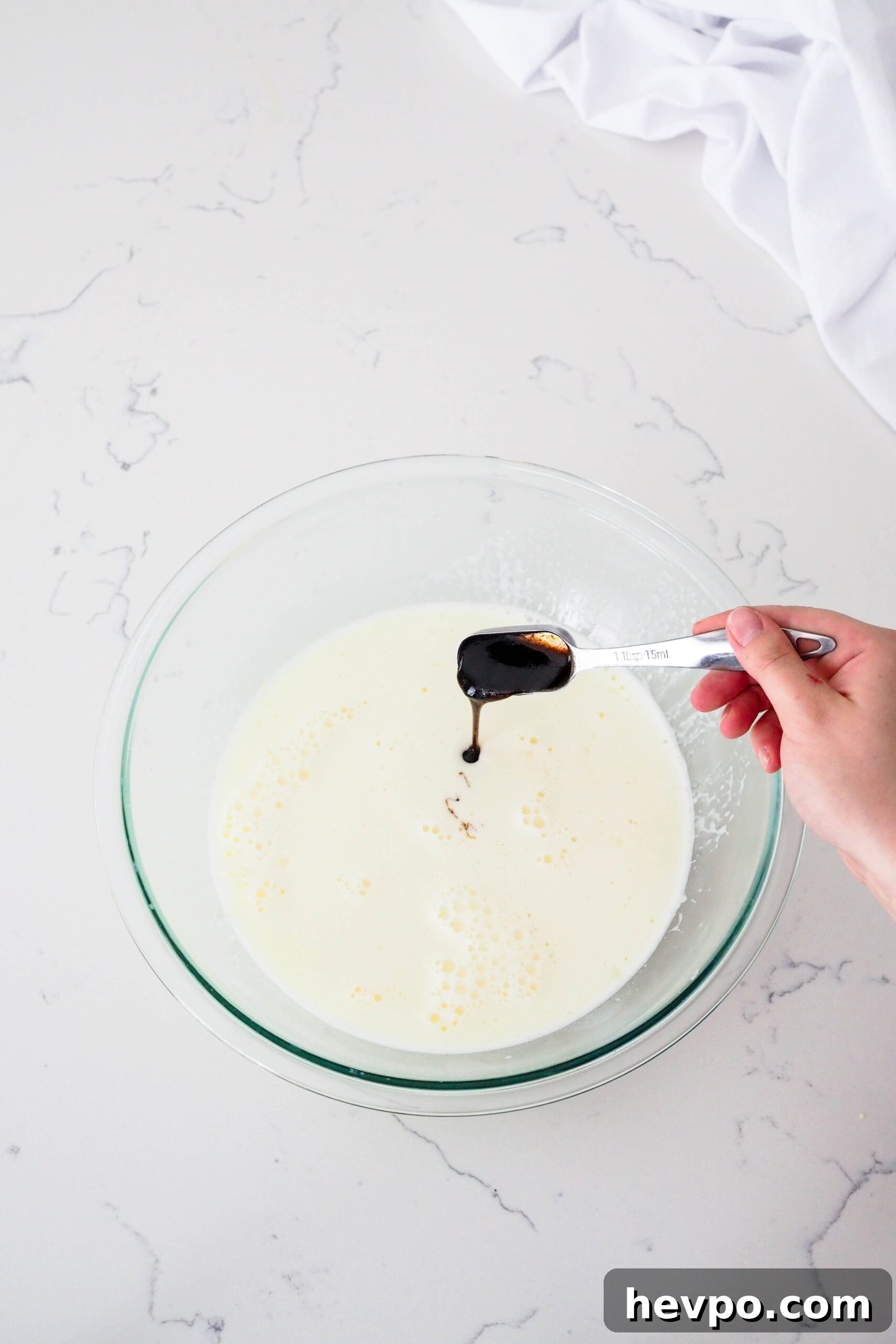 Homemade French Vanilla Ice Cream Recipe – Creamy & Classic 9 A hand pours a Tablespoon of vanilla bean paste into ice cream custard.