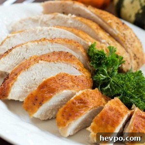 Sliced roasted turkey breast with golden brown skin on a white plate garnished with parsley