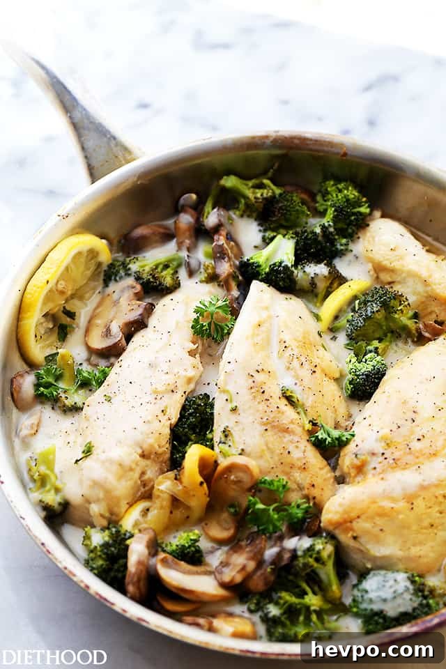 Creamy chicken Alfredo with broccoli in a skillet, garnished with lemon slices.