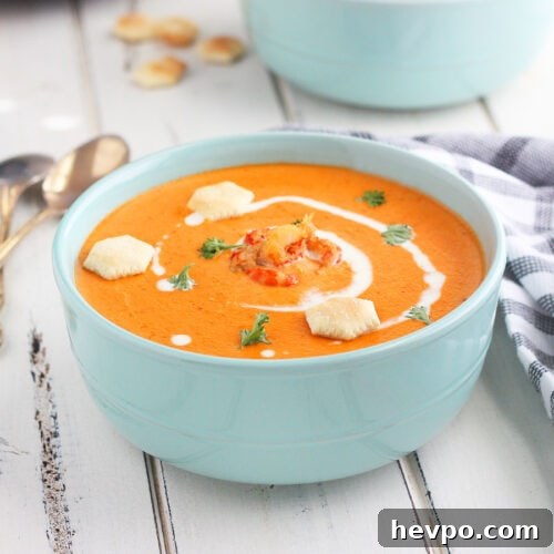 Bowl of crawfish bisque garnished with cream, parsley and oyster crackers on a white wooden background.