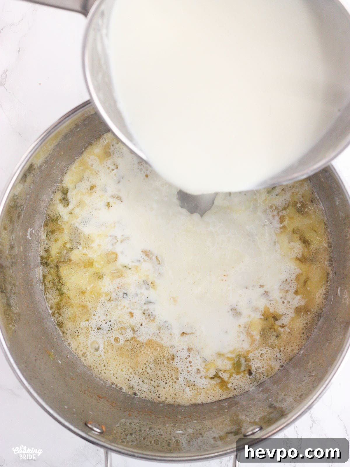 milk and heavy cream being poured from a saucepan into a stockpot of sautéed vegetables