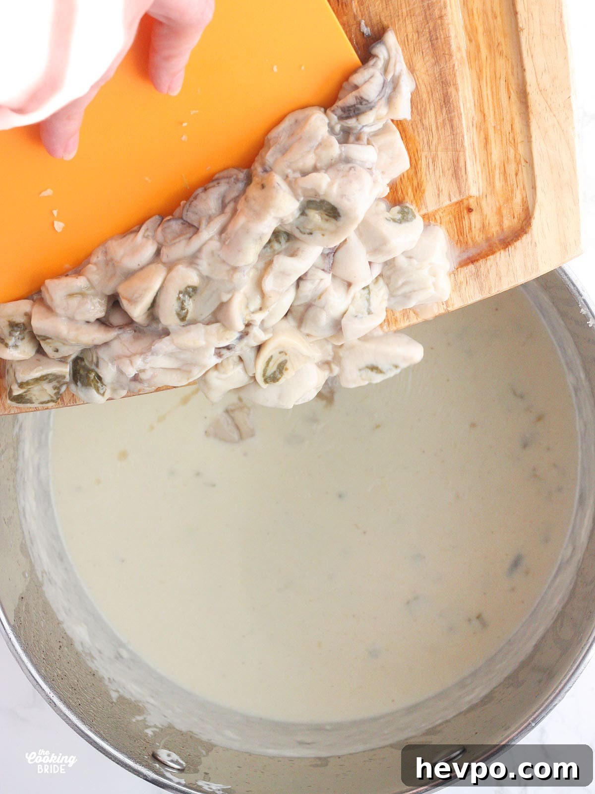 hand pushing raw oysters off of a cutting board and into a pot of heavy cream and milk