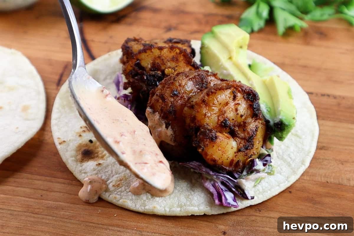 Spicy Blackened Shrimp Tacos with Avocado Lime Slaw 13 assembling shrimp taco, adding sauce to one side of the shrimp.