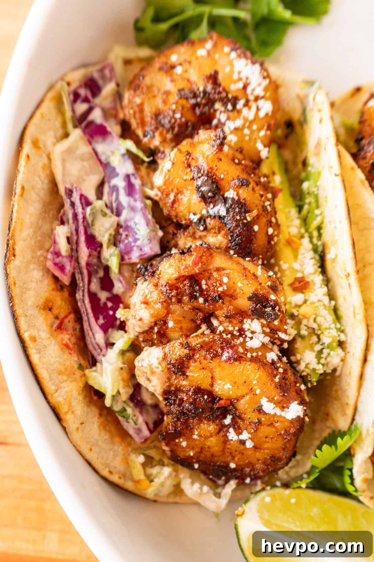 Spicy Blackened Shrimp Tacos with Avocado Lime Slaw 14 shrimp taco filled with shrimp and all the toppings, sitting on white plate next to lime wedge.