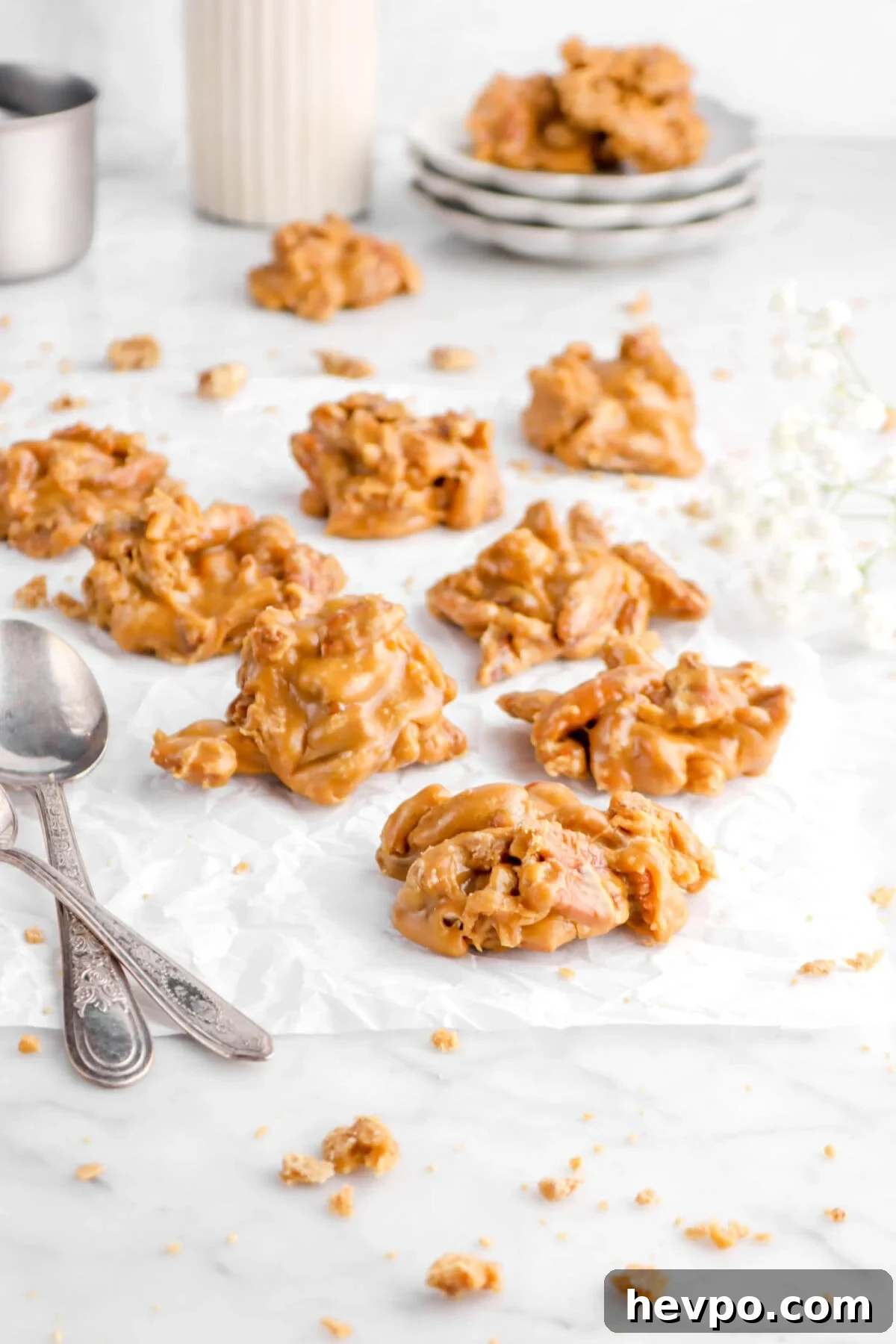 Southern Buttermilk Pecan Pralines Recipe – Classic Southern Candy 2 pecan pralines on parchment paper with two spoons and flowers behind
