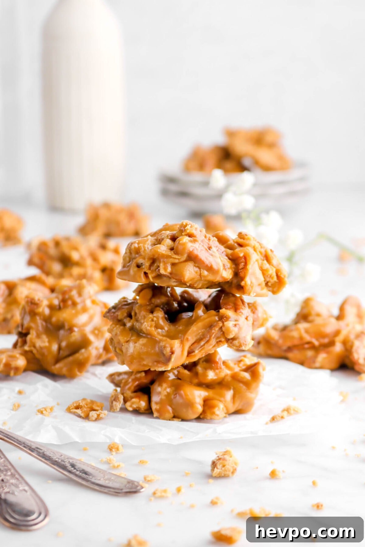 Southern Buttermilk Pecan Pralines Recipe – Classic Southern Candy 14 stacked pralines on parchment with more behind and white flowers