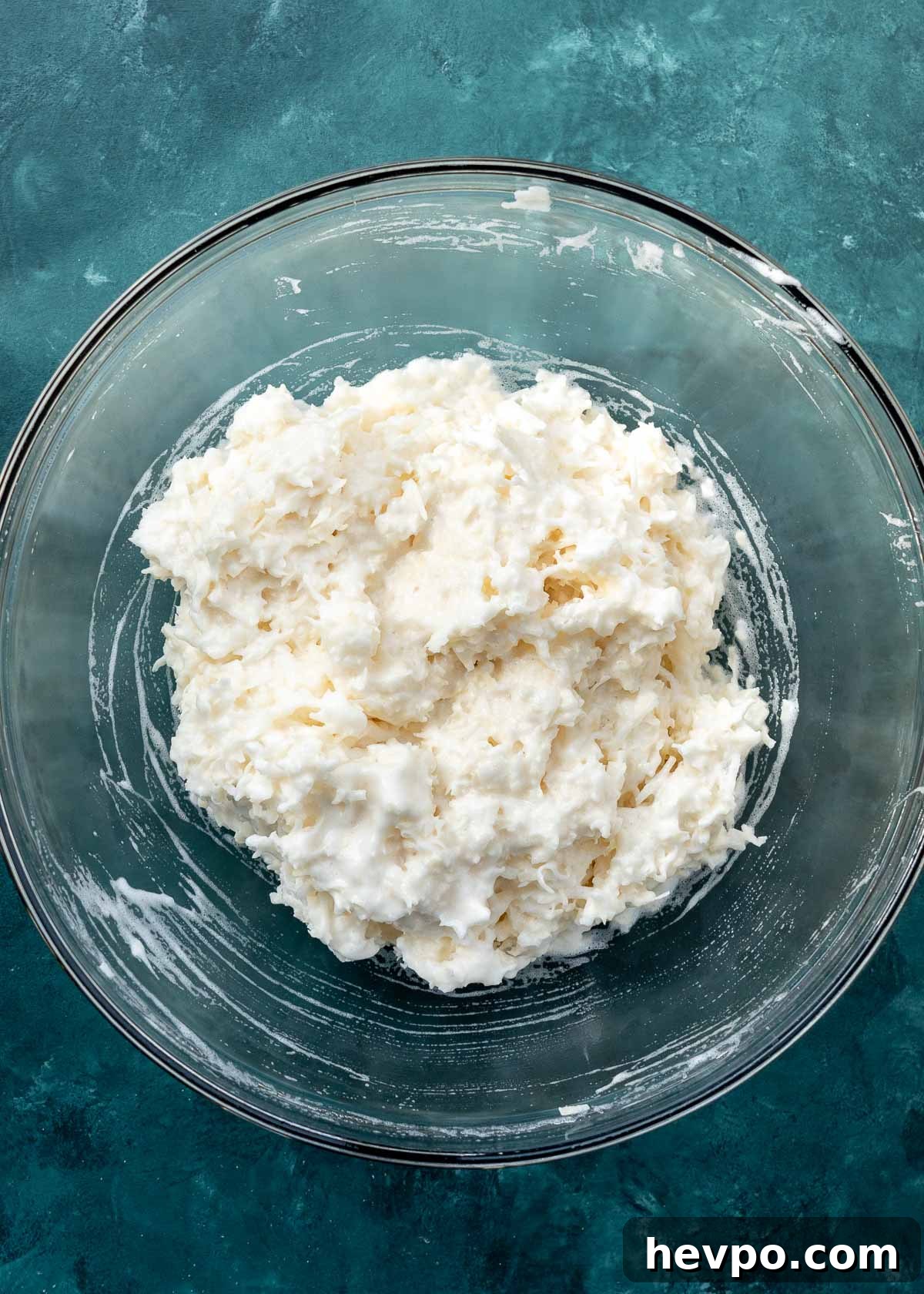 overhead shot of coconut being added to macaroons in clear mixing bowl
