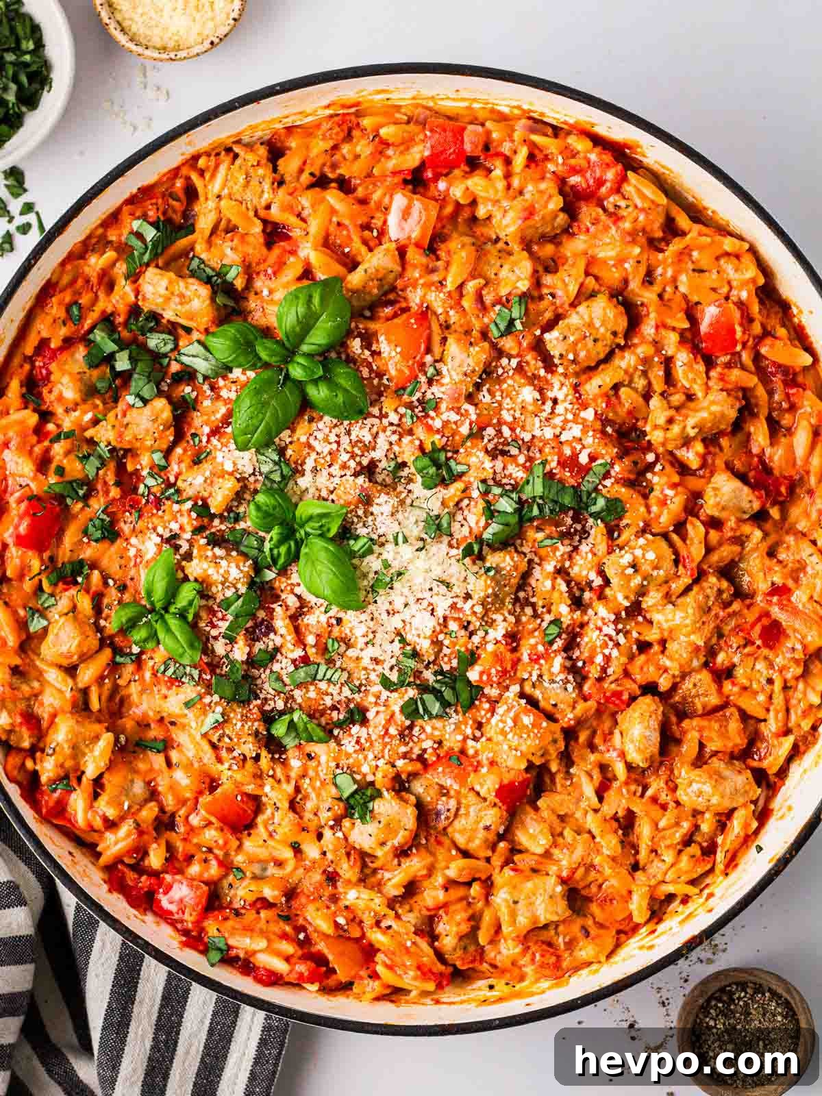 One-Pot Sausage and Orzo Dinner 2 A big white pan on a white counter filled with Sausage Orzo in a tomatoey sauce and basil on top.