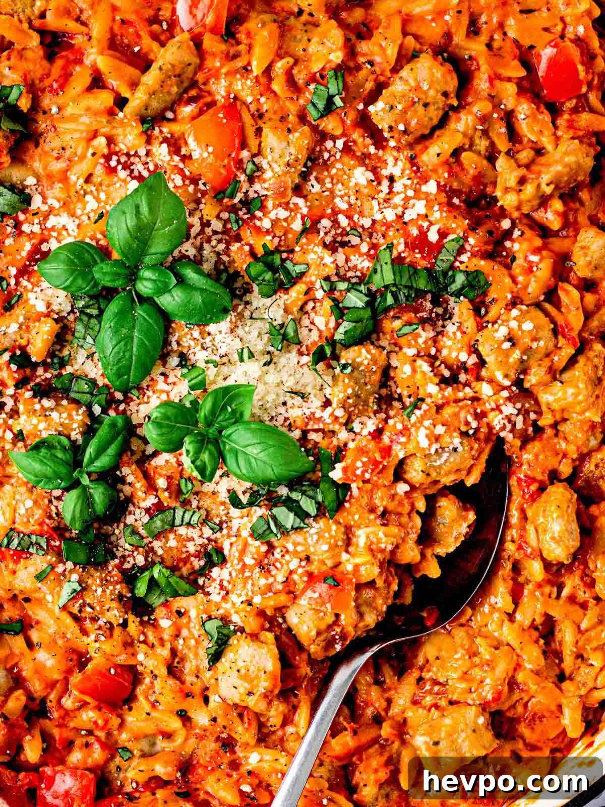 One-Pot Sausage and Orzo Dinner 3 A close up of Sausage Orzo pasta with a spoon and basil on top.