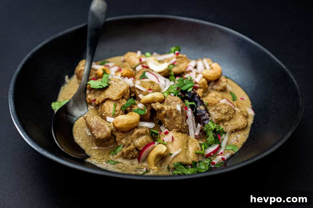 Top 10 Most Popular Recipes of 2022 You Need to Try 8 Bengali Rezala Chicken in a black bowl with spoon on a black background.
