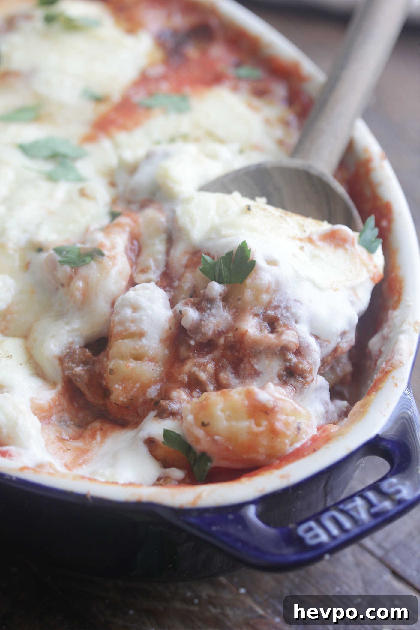 Close up scoop of Gnocchi Lasagna in a dark blue baking dish with melted cheese on top