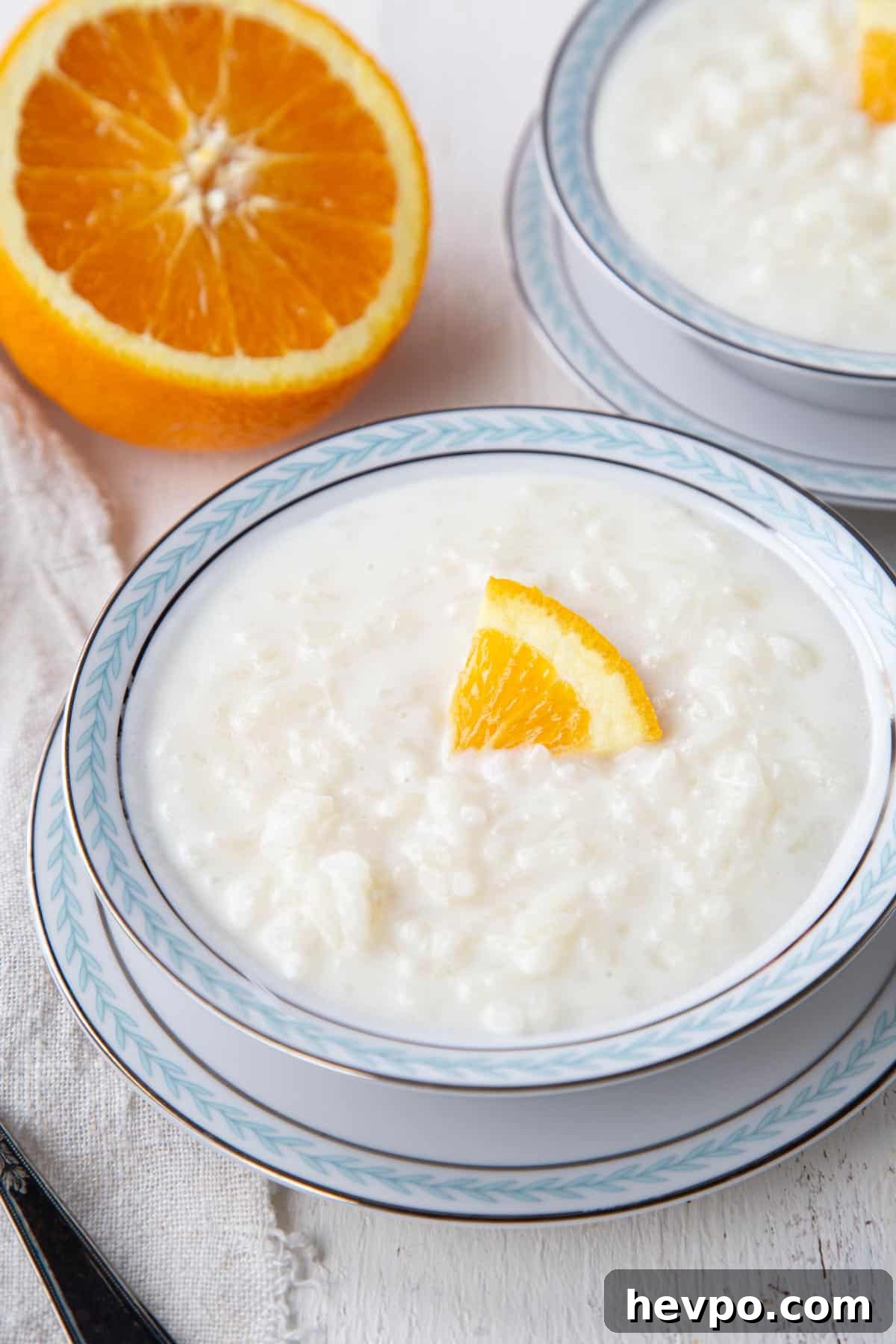 Creamy Rice Pudding Made with Cooked Rice 2 bowl of rice in a creamy white pudding, topped with a slice of orange.