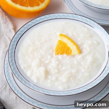 Creamy Rice Pudding Made with Cooked Rice 10 rice pudding in a decorative blue and white bowl, topped with a slice of orange.