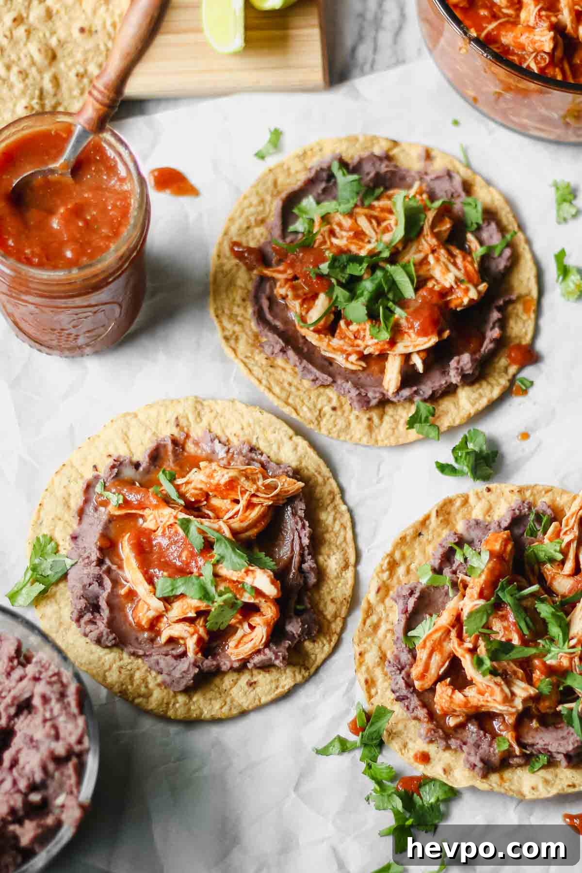 Chicken Tinga Tostadas — Instant Pot or Slow Cooker Guide 2 Three tostadas topped with a layer of refried black beans and shredded chicken Tinga, garnished with cilantro.