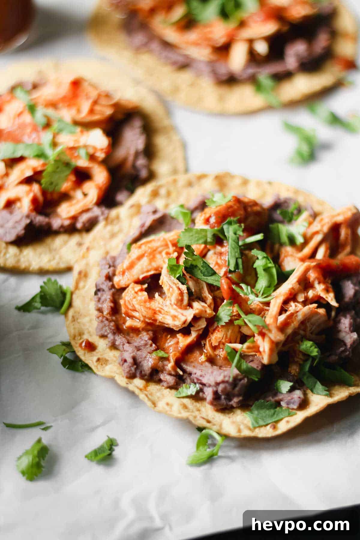 Chicken Tinga Tostadas — Instant Pot or Slow Cooker Guide 5 Shredded chicken Tinga on top of a tostada with refried beans and cilantro.