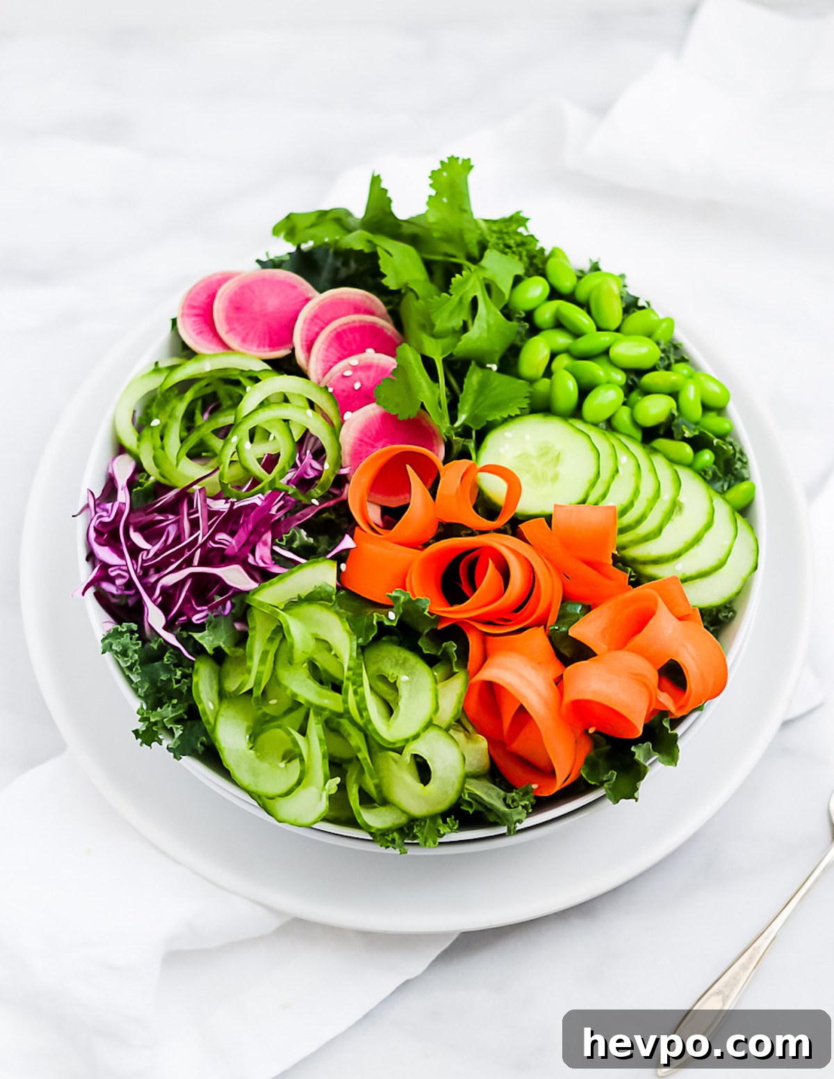 A large kale salad topped with carrots, cucumbers, radishes, cabbage, and edamame.