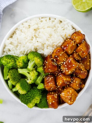 A white bowl holding sesame tofu, white rice, and broccoli.
