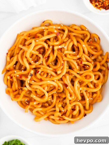 A white bowl of noodles that are covered in white sesame seeds and red pepper flakes.