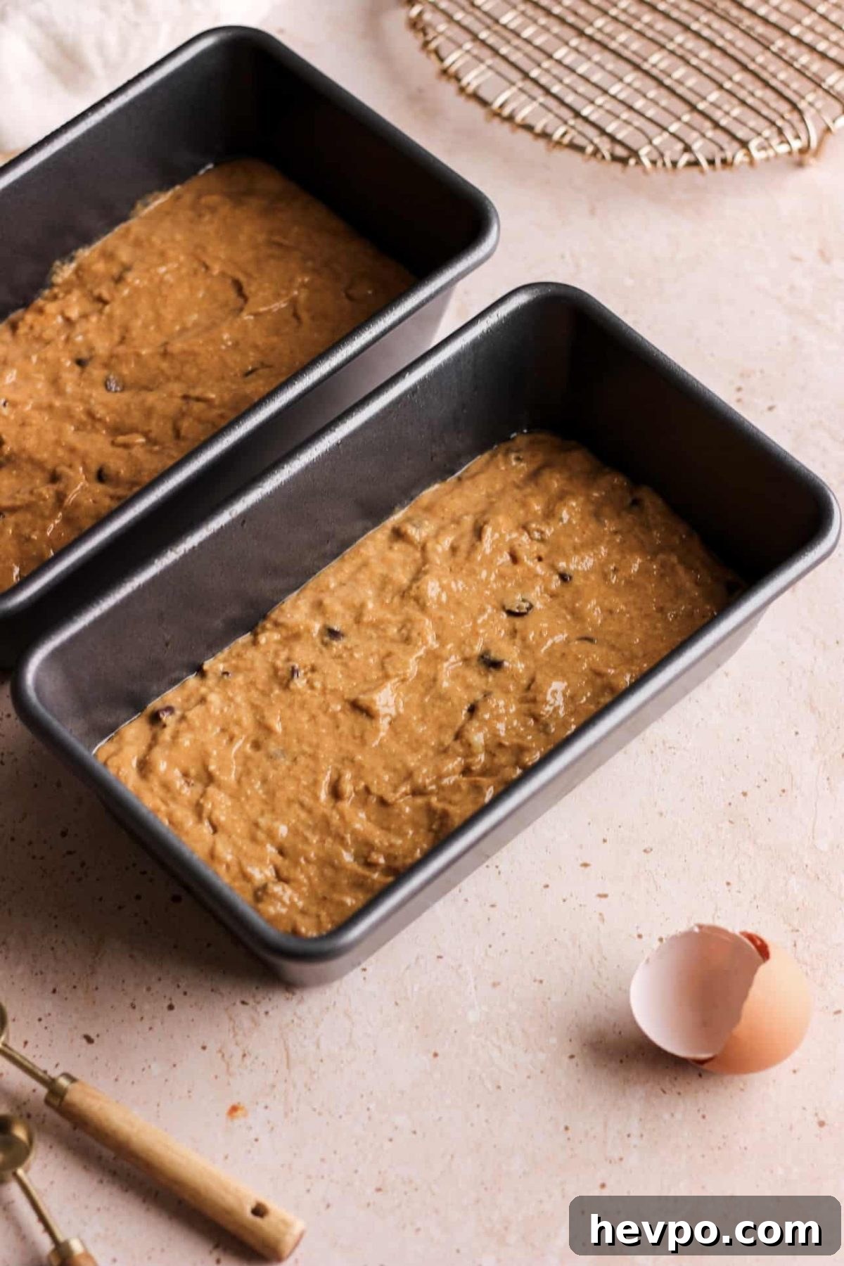 two loaf pans halfway filled with pumpkin banana bread batter and an egg shell for food photography