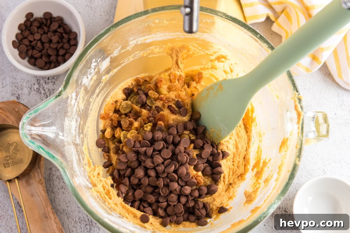 adding chocolate chips and raisins to pumpkin muffin batter