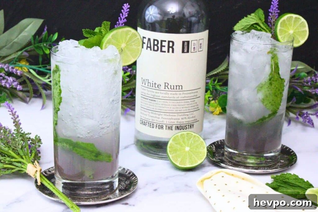 two lavender mojitos in tall glasses with crushed ice garnished with lime wheel and mint surrounding rum bottle