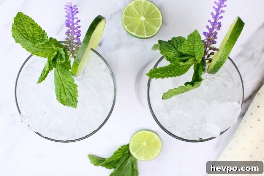 overhead view of two lavender mojito drinks with crushed ice lime and mint on white marble counter