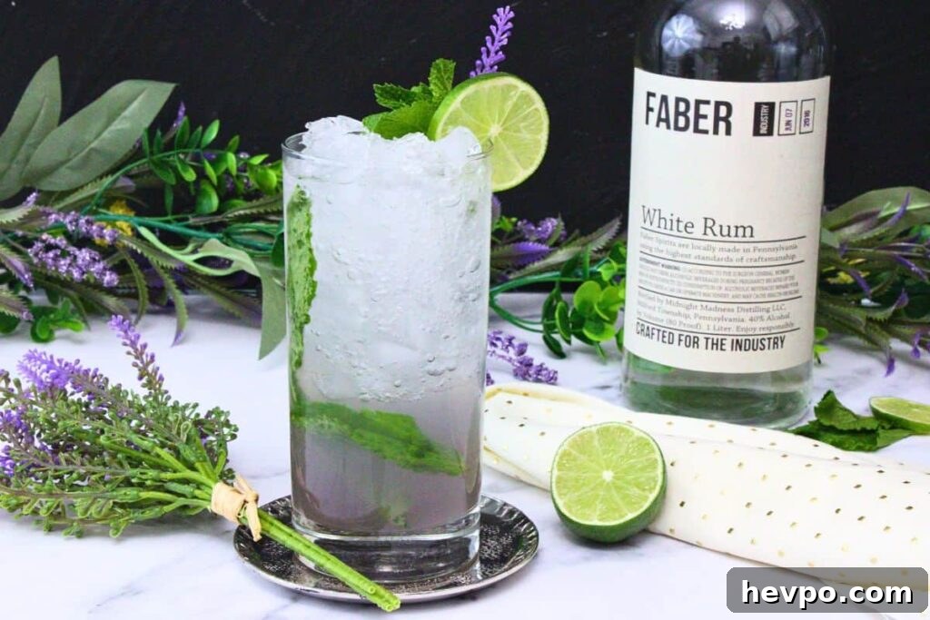 lavender mojito in a tall glass garnished with lime and mint next to rum bottle