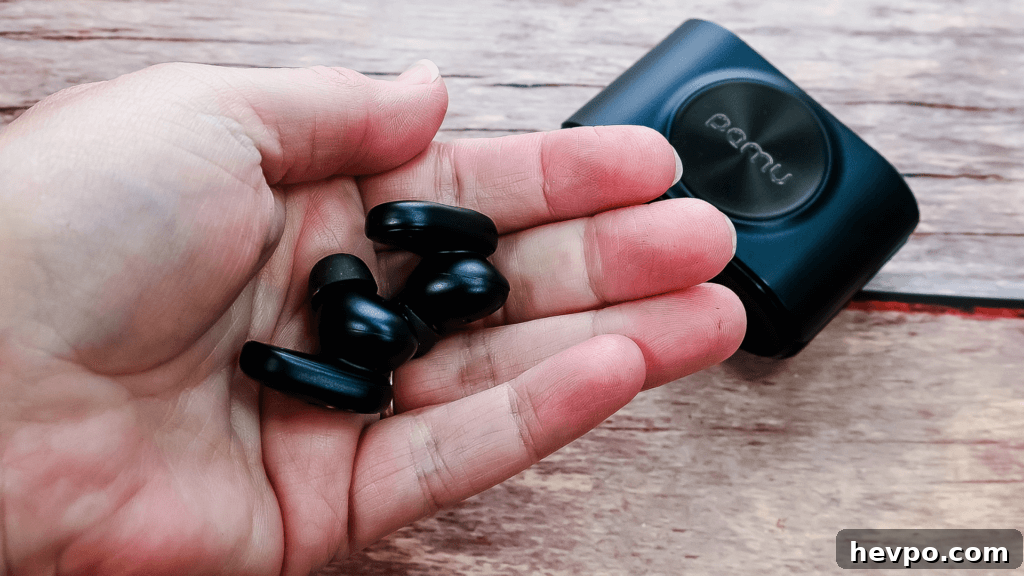 A hand holding the PaMu Slide 2 ANC Wireless Earbuds with the case behind them.