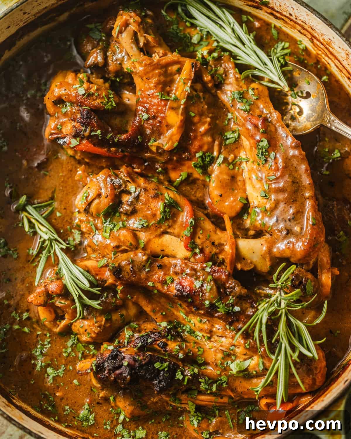 up close photo of smothered turkey wings in a pot garnished with rosemary. 