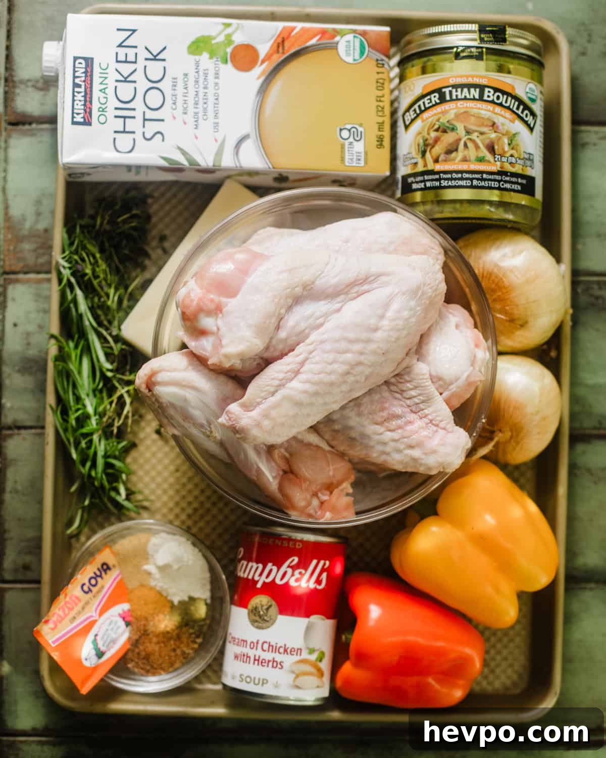 ingredients to make smothered turkey wings on a baking sheet - turkey wings, onion, fresh herbs, celery, garlic, bell pepper, cream of chicken soup, seasonings, chicken broth, chicken bouillon paste, dijon mustard, worcestershire sauce, bay leaves, bacon, and butter.