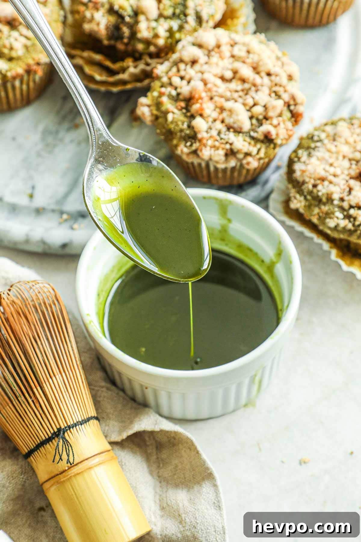Spoon pouring matcha vanilla bean glaze for cakes, muffins, quick breads, and more in a white ceramic ramekin.