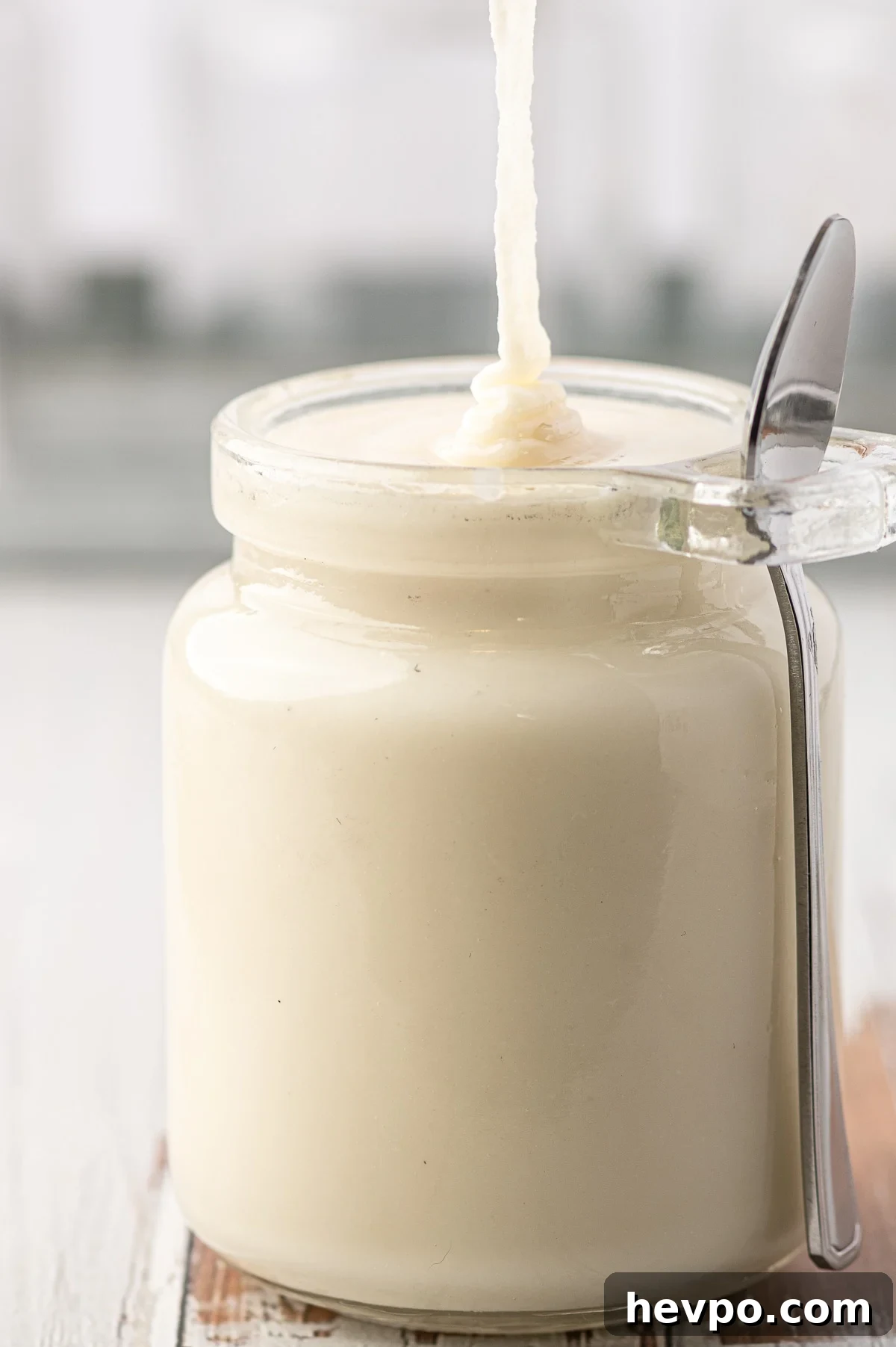 Just made low carb coconut butter being poured into a glass jar against a grey background 