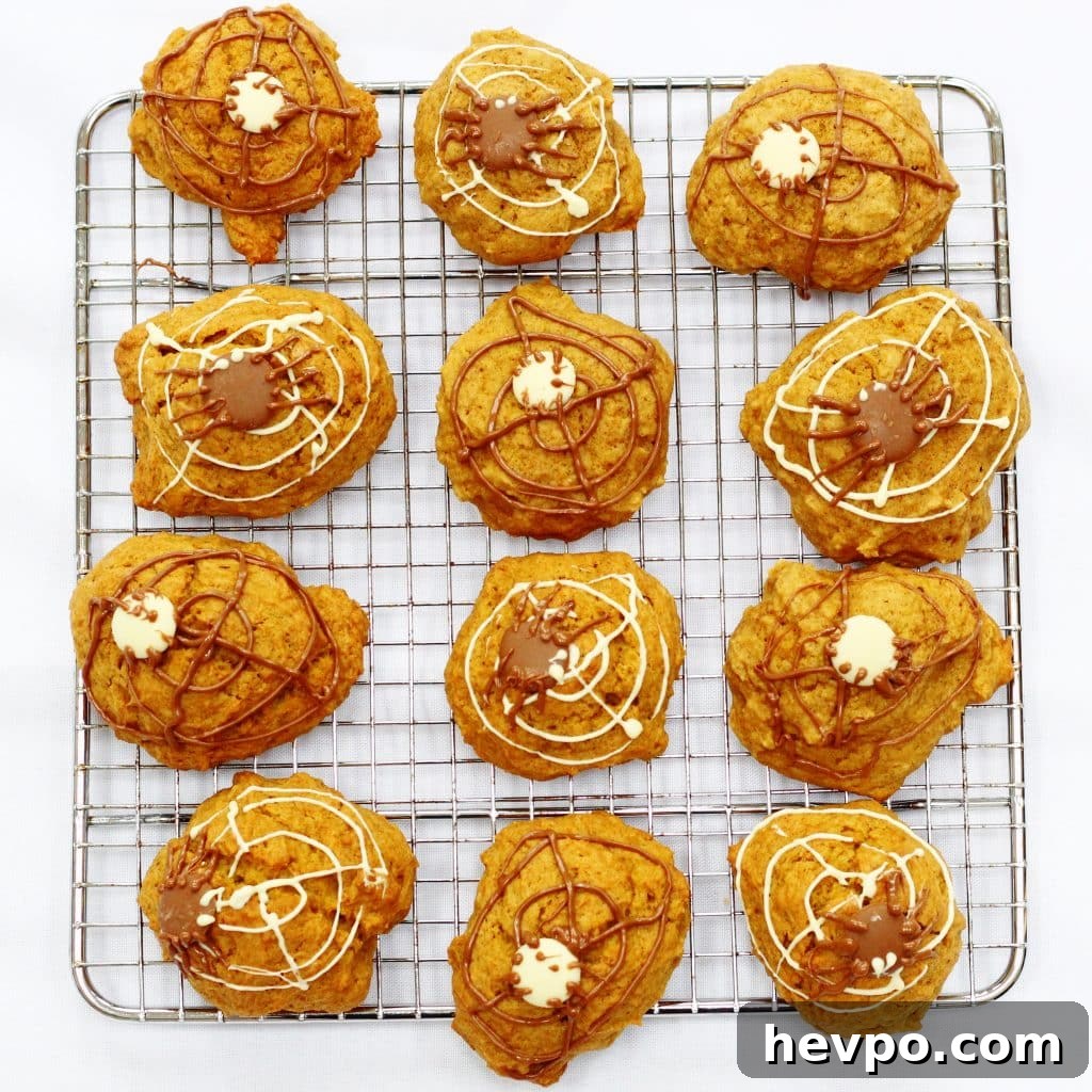 Pumpkin cookies on a cooling rack, decorated with chocolate spiders and webs