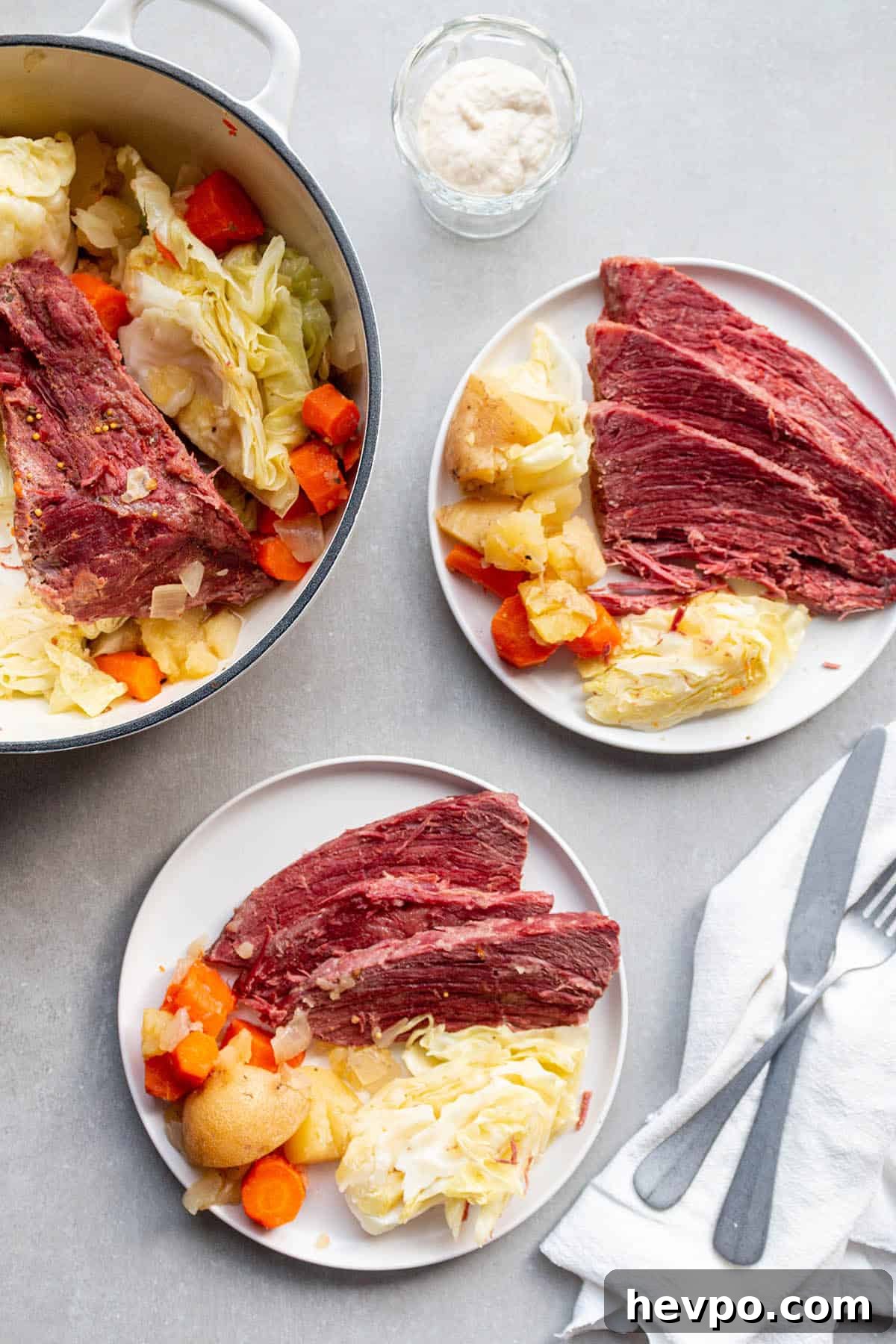 Two plates with servings of corned beef, cabbage, carrots and potatoes with a Dutch Oven full of the roast.