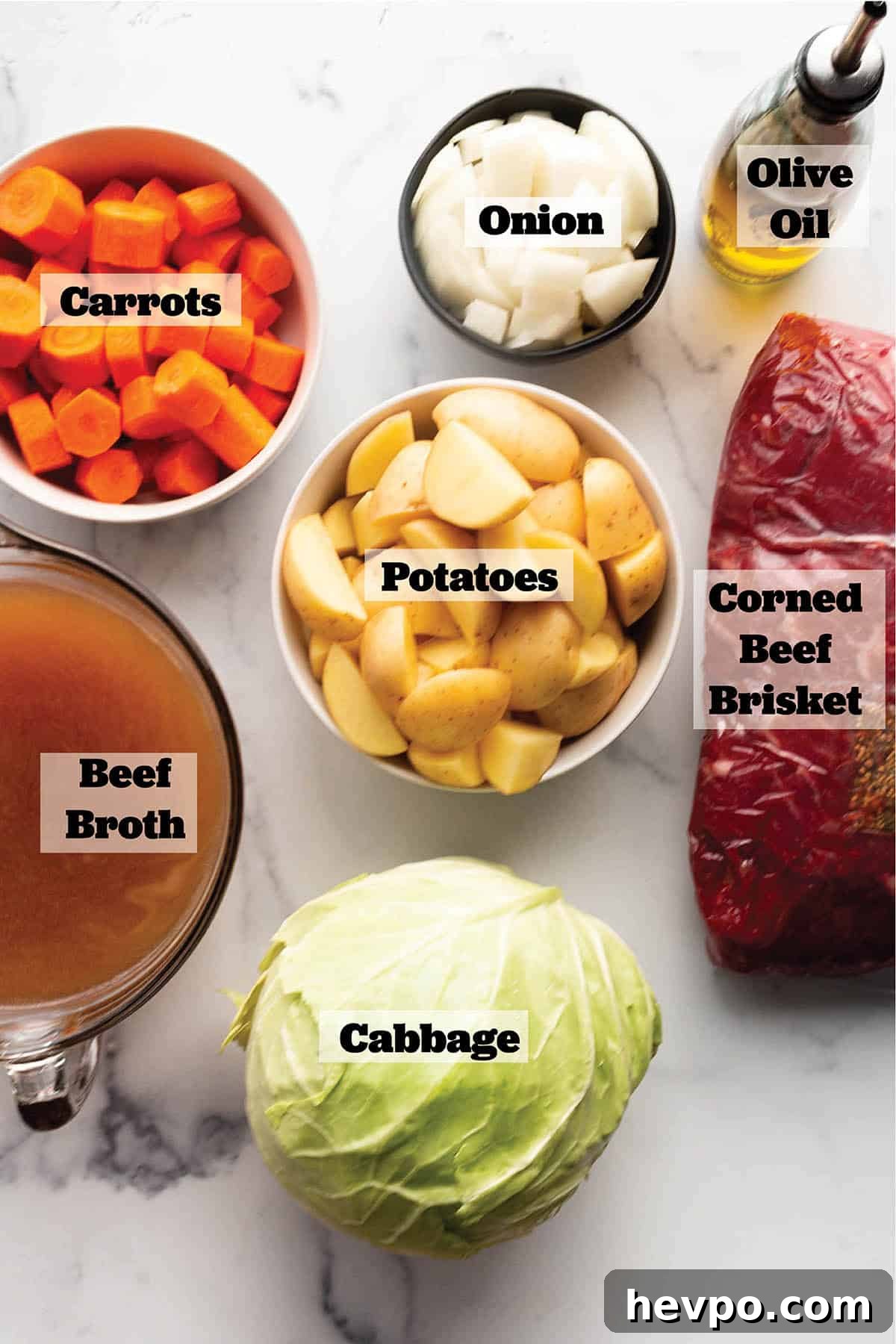 Prep bowls with chopped carrots, onions, potatoes, a head of cabbage, bowl of beef broth and a corned beef brisket and olive oil.