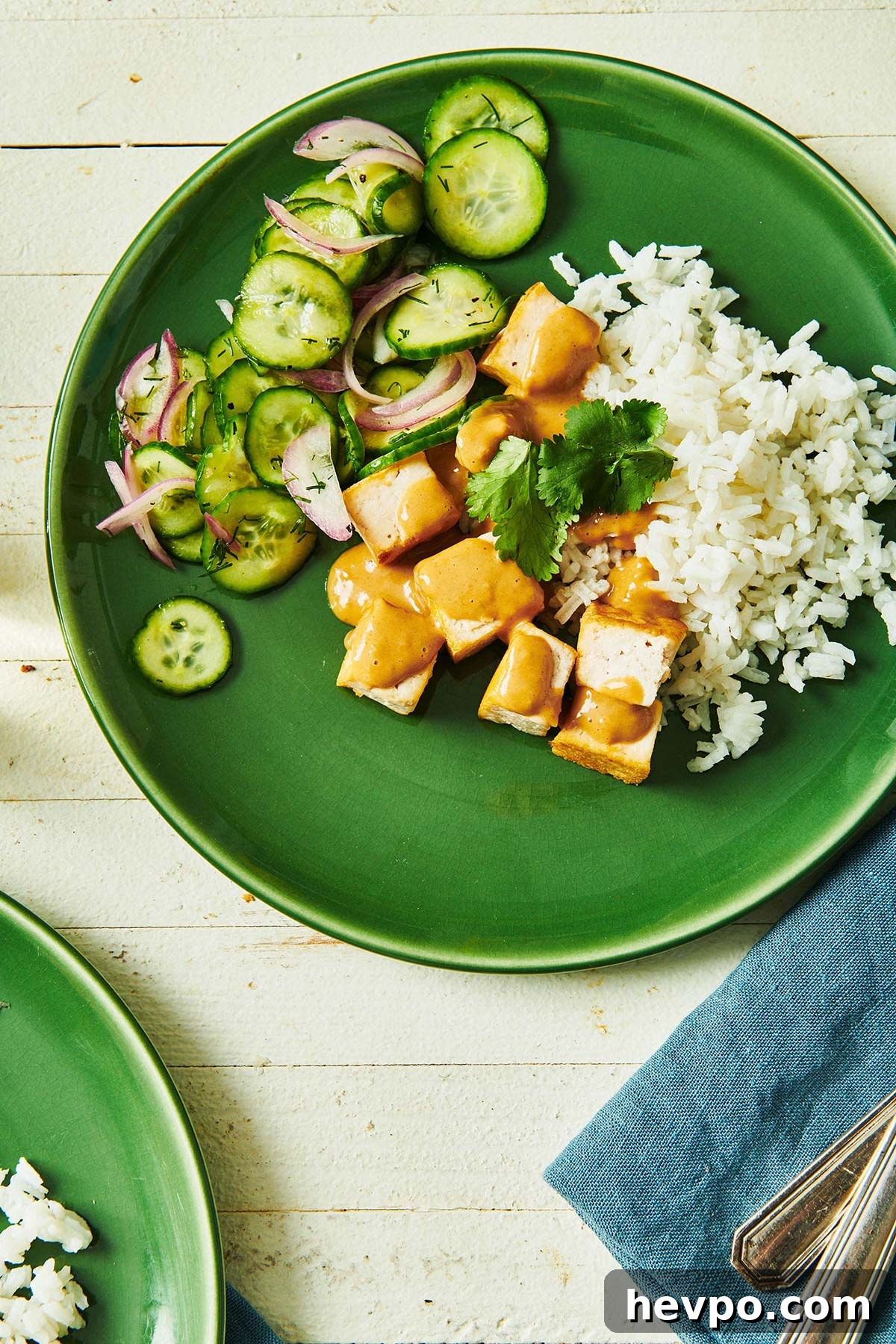 How to Press Tofu for Firmer, Crispier Results 2 Tofu with Peanut Sauce on a green plate with rice and cucumber salad.
