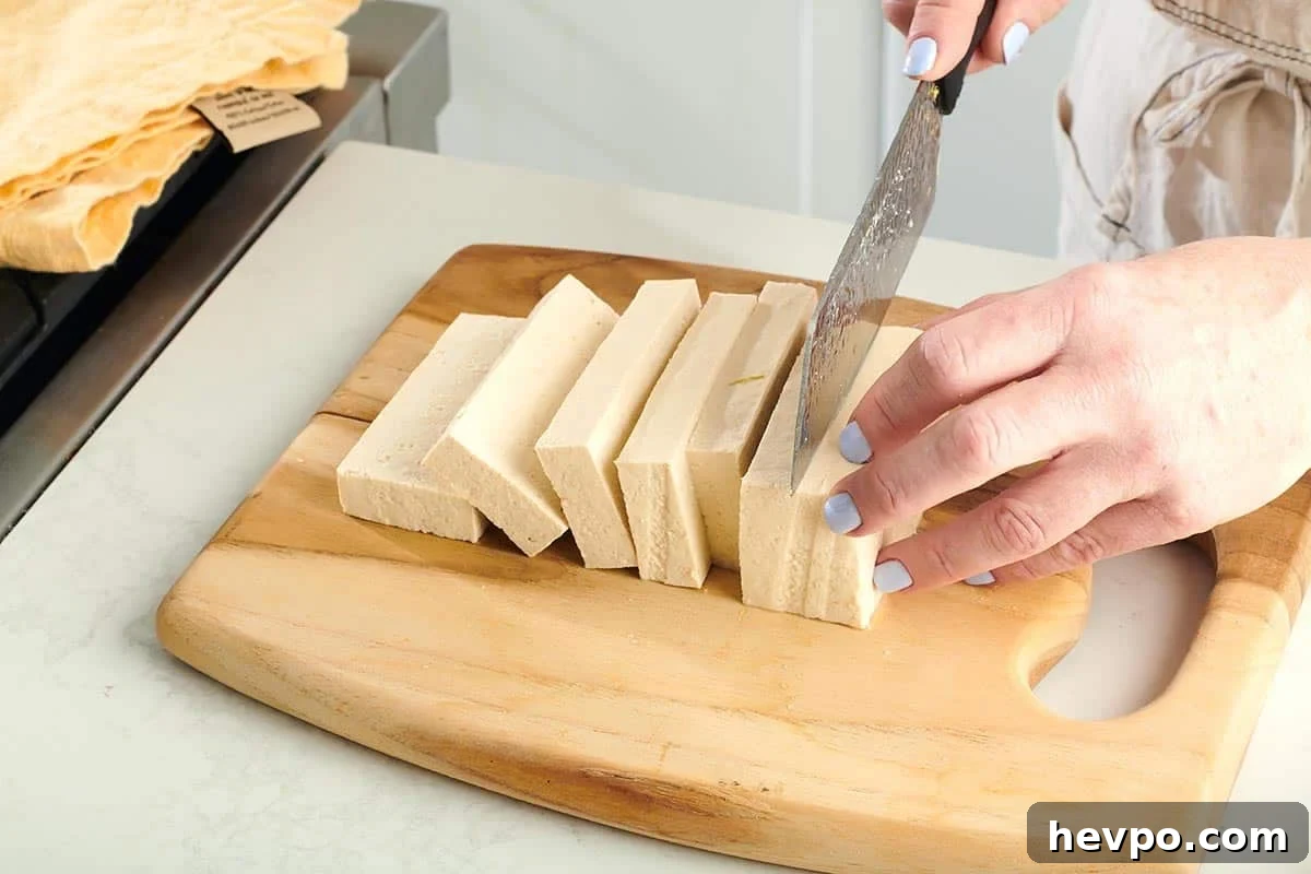 How to Press Tofu for Firmer, Crispier Results 6 Woman slicing tofu on a wooden cutting board.