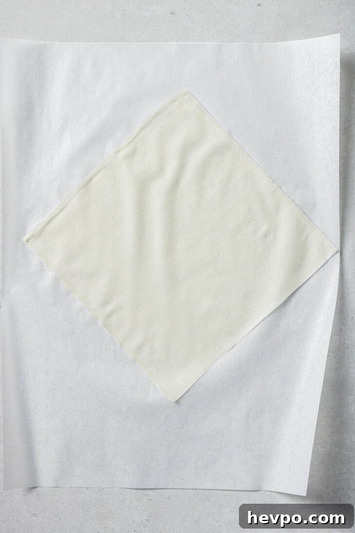 One pastry sheet laid on the diagonal on top of a piece of parchment paper ready to be filled to make Chicken Spring Rolls.