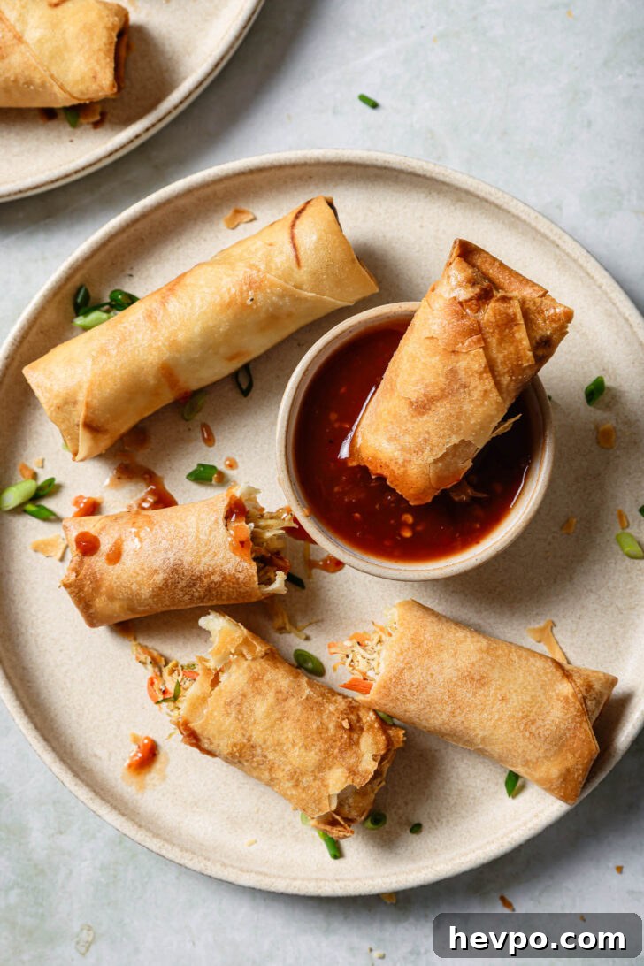 Half eaten Chicken Spring Rolls on a plate with one half dipped in the sauce.