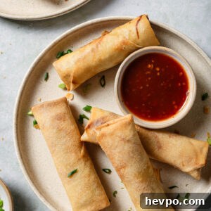 Chicken Spring Rolls on a round plate with a small bowl of dipping sauce ready to be eaten.