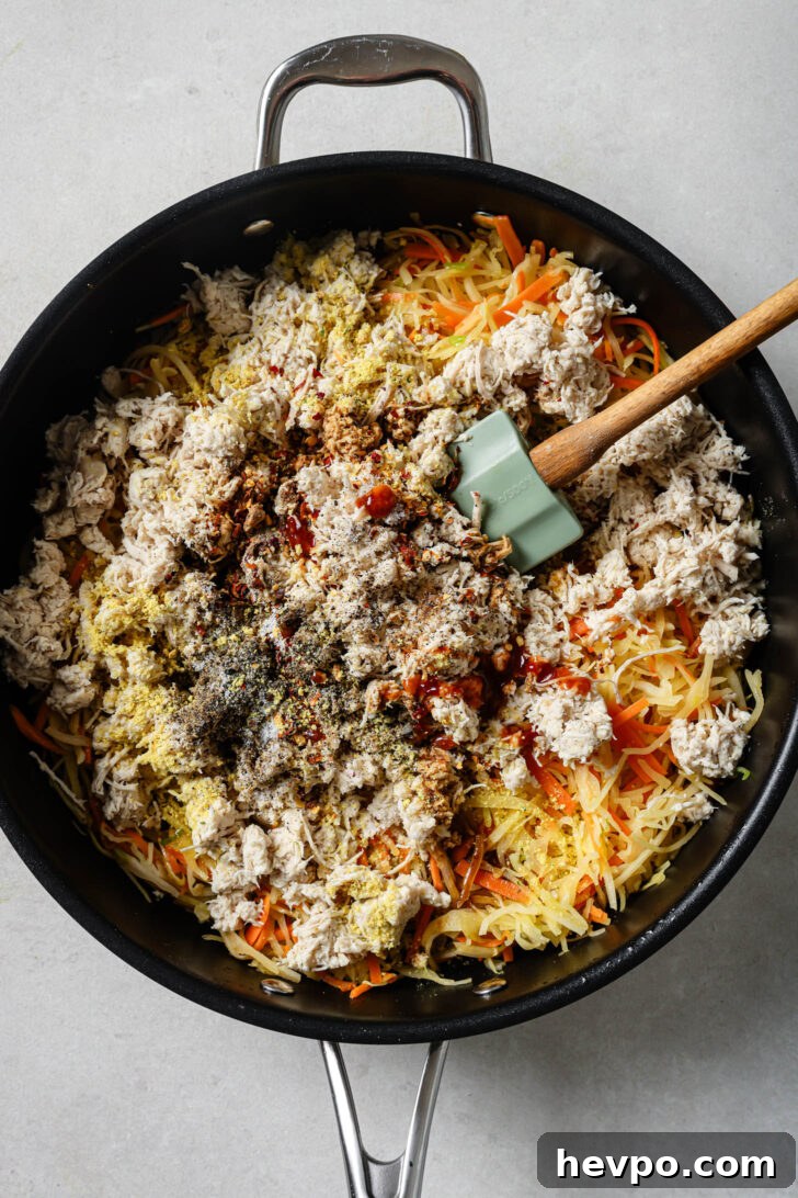 Mixing together sauteed vegetables, shredded chicken and spices in a skillet to make the filling for Chicken Spring Rolls.