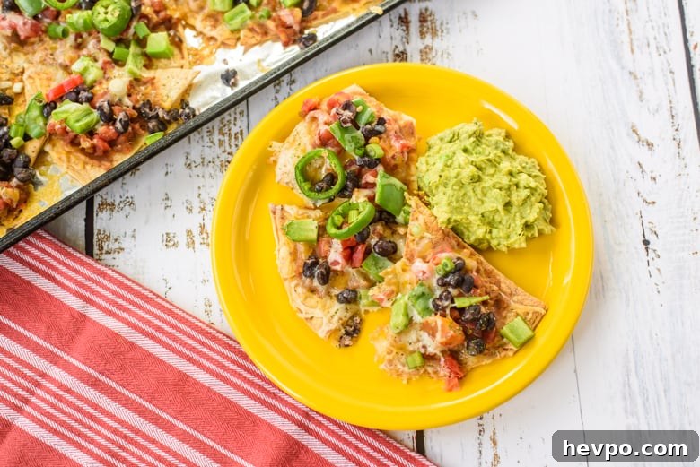 Nachos with beans, peppers, and melted cheese on yellow plate with guacamole on the side
