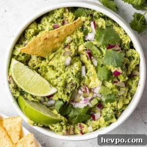 Round white bowl filled with guacamole, one chip dipped in.