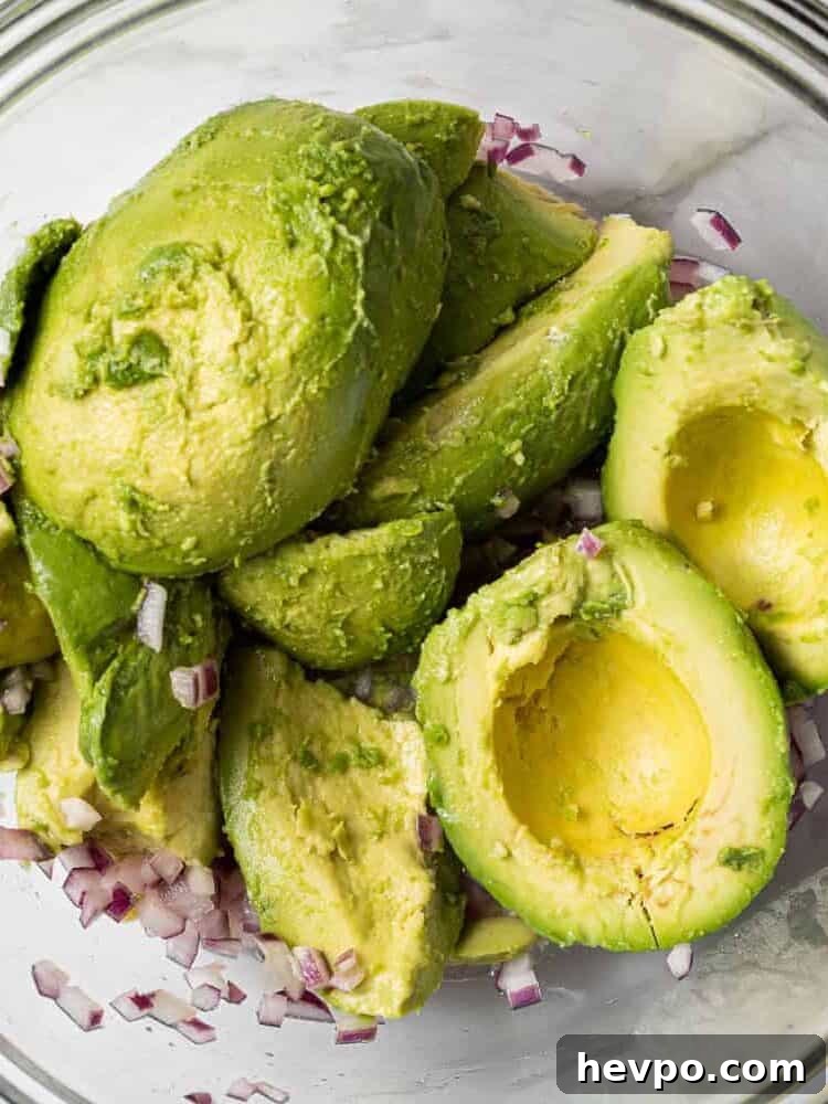Peeled avocado halves in a bowl with red onions.