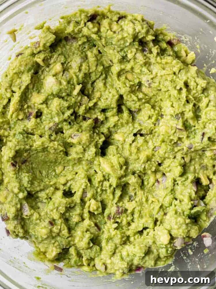 Mashed avocado in a clear glass bowl.