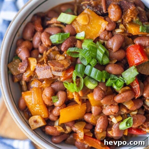 A bowl of delicious Mexican beans mixed with diced bell peppers, onions, and topped with chopped green onions.