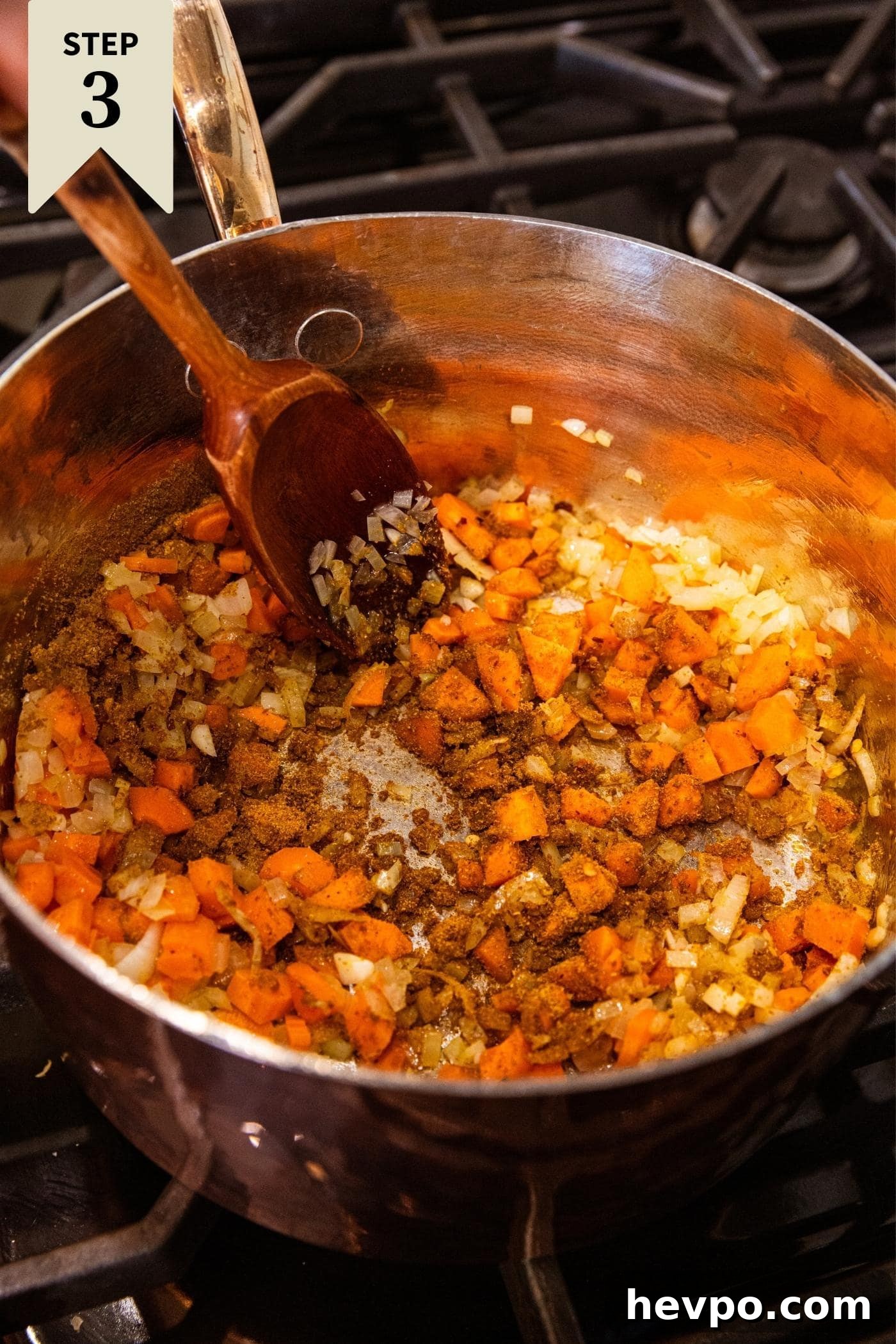 Wooden spatula in copper pot mixing in spices with carrots and onions.